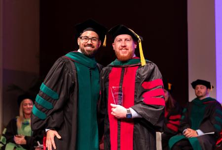 Image of Dr. Jacob Ribbing presenting Dr. Joshua Reeves with the Excellence in Scholarship Award