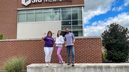 Image of Staci Eakins, Victoria Halfacre and Dr. Jacob Ribbing standing outside of the Carbondale Family Medicine Clinic showing off their Doctor of Medical Science Apparel