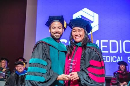 Image of Dr. Jacob Ribbing posing with Dr. Annie Kowalis and her Excellence in Scholarship Award at the 2024 SIU DMSc Hooding Ceremony