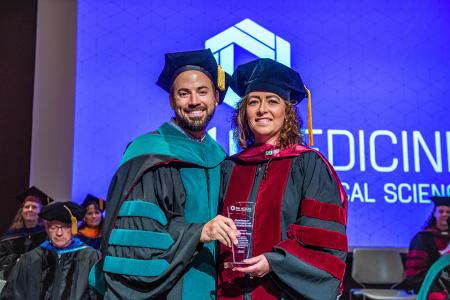 Image of Dr. Jacob Ribbing and Dr. Cassandra Wood with her Leadership and Advocacy Award at the 2024 SIU DMSc Hooding Ceremony