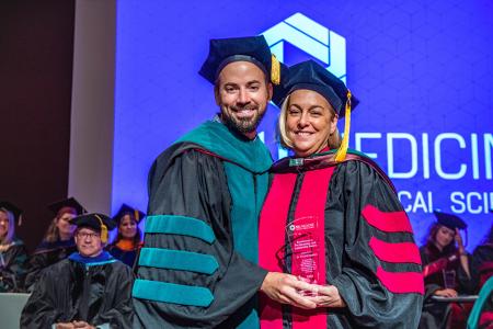 Image of Dr. Jacob Ribbing and Dr. Deborah Epstein with her Leadership and Advocacy Award at the 2024 SIU DMSc Hooding Ceremony