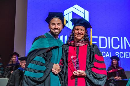 Image of Dr. Jacob Ribbing and Dr. Jodi Wernikoff with her Advocacy and Leadership Award at the 2024 SIU DMSc Hooding Ceremony