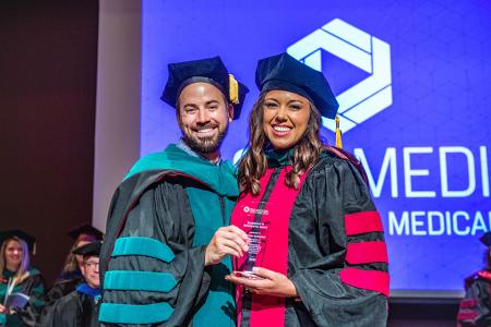 Image of Dr. Jacob Ribbing and Dr. L. Kristen Schloemann with her Excellence in Scholarship Award at the 2024 SIU DMSc Hooding Ceremony